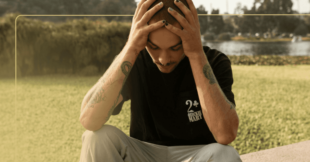 man experiencing trauma-related anger, sitting on the ground holding head in frustration