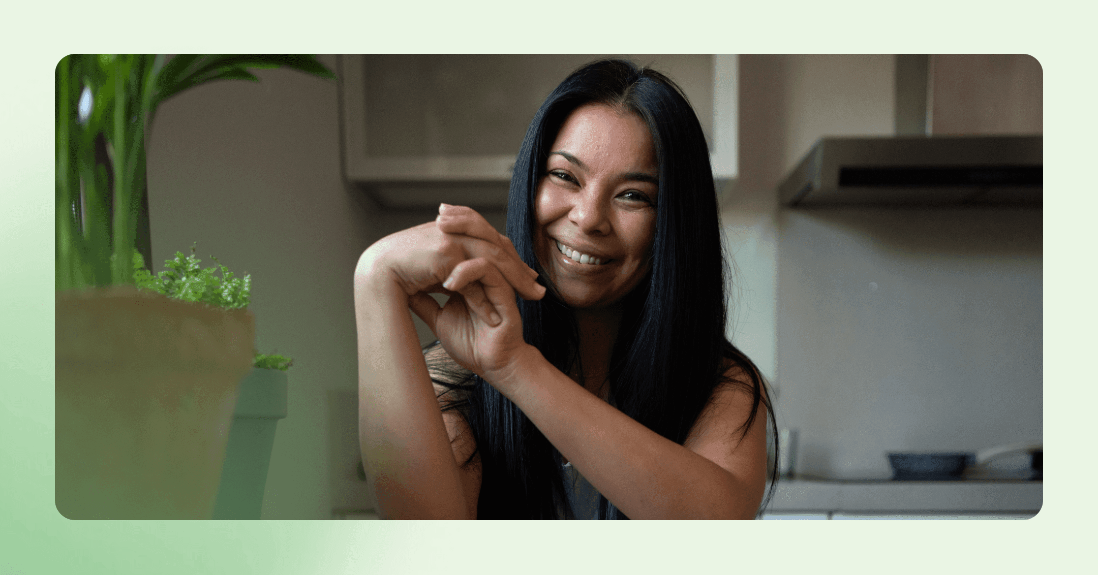 image of a woman with dark hair sitting at a kitchen table. She has a big smile and there is a kitchen out of focus in the background.